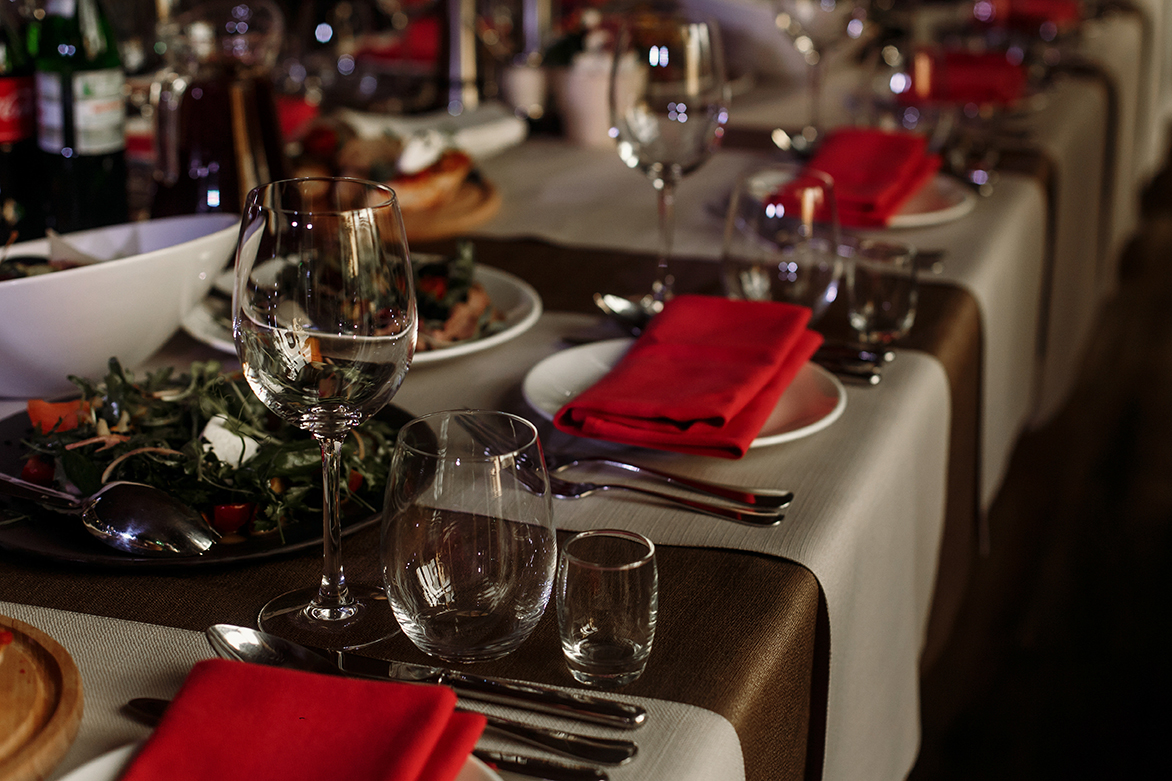 Luxury wine glasses and silver tableware near plates with red napkins close-up - wedding reception table arrangement, brown, rustic tablecloth background, special occasion catering concept